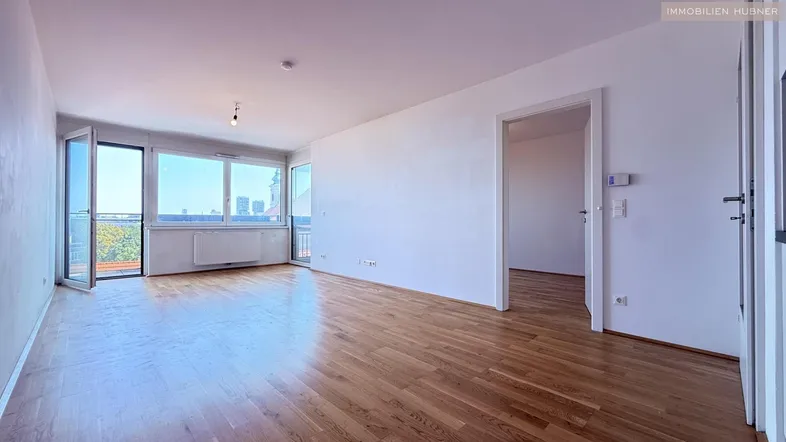 Helles Wohnzimmer mit Holzboden, großen Fenstern und Zugang zu einem Balkon.