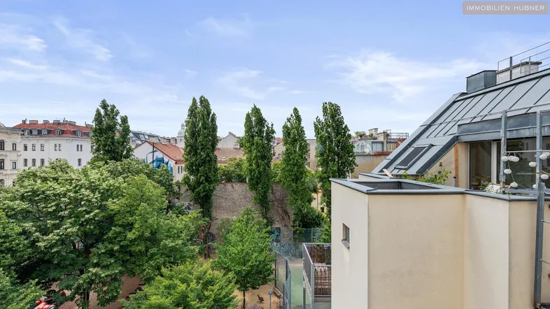 Blick von einer oberen Etage auf einen grünen Innenhof mit Bäumen und umliegenden Gebäuden.