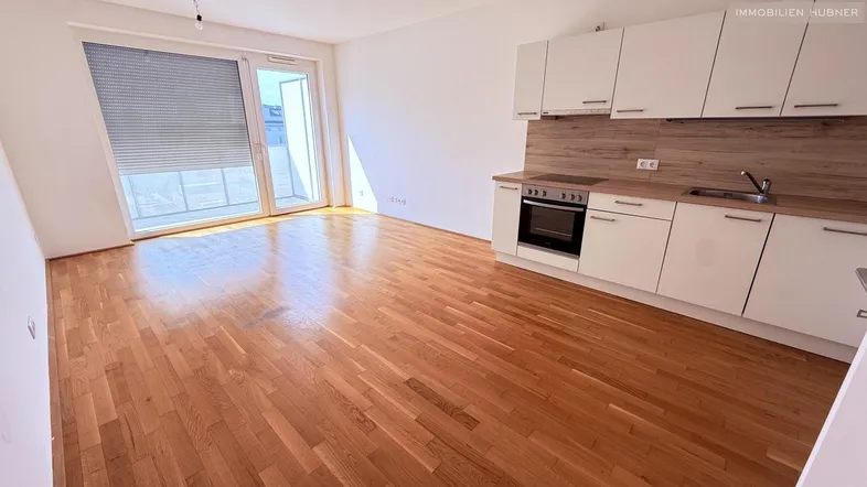 Heller Wohn-Essbereich mit integrierter Küche, Parkettboden und Zugang zum Balkon.