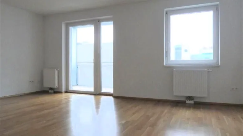 Helles Zimmer mit Parkettboden, weißen Wänden und Zugang zu einem Balkon, ideal für individuelle Gestaltung.