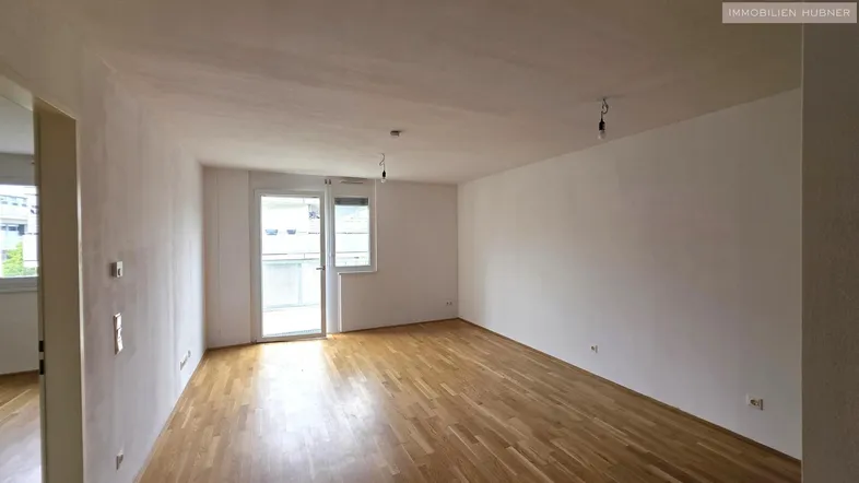 Helles Zimmer mit Parkettboden und Zugang zu einem Balkon, ideal als Wohn- oder Schlafbereich.