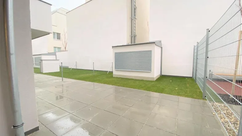 Gepflasterte Terrasse mit angrenzender Rasenfläche und Blick auf moderne Gebäudefassaden.