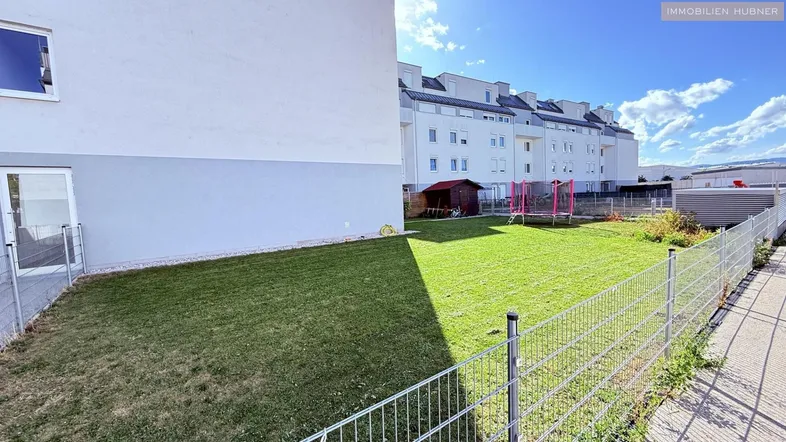 Grüner Gartenbereich neben einem modernen Gebäude mit Trampolin und Gartenhaus.