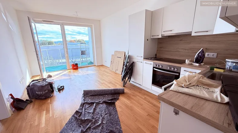 Helles Wohnzimmer mit offener Küche, Parkettboden und Zugang zum Balkon mit Weitblick.