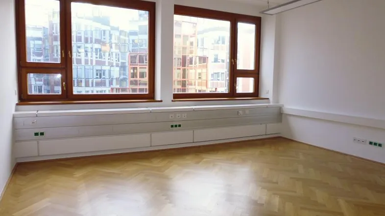 Heller Büroraum mit Fischgrätparkett, großen Holzfenstern und integrierten Wandsteckdosen.