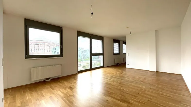 Helles Wohnzimmer mit Parkettboden und großen Fenstern, die viel Tageslicht hereinlassen.