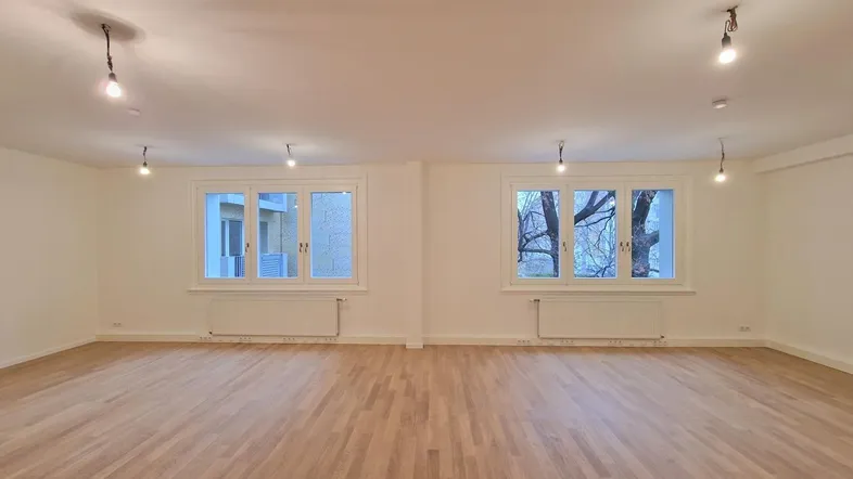 Heller, leerer Raum mit Holzboden und zwei Fenstern, bereit zur individuellen Gestaltung und Nutzung.