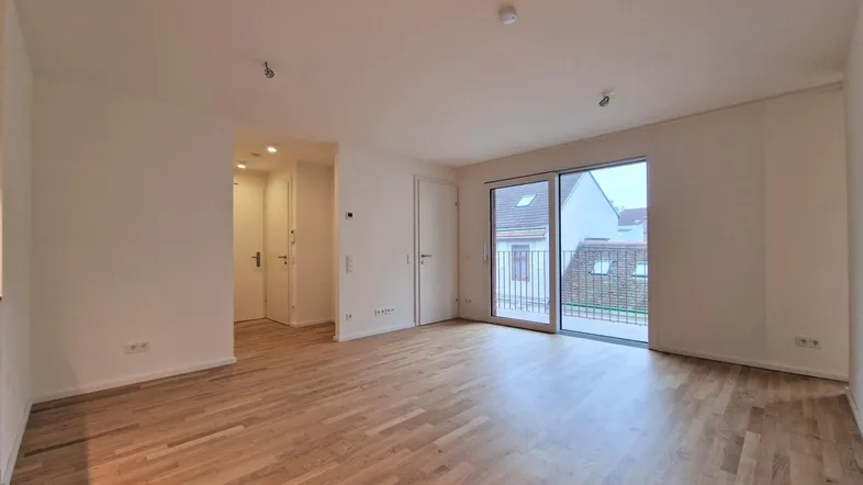Helles Wohnzimmer mit Parkettboden und Zugang zum Balkon, unmöbliert und geräumig.