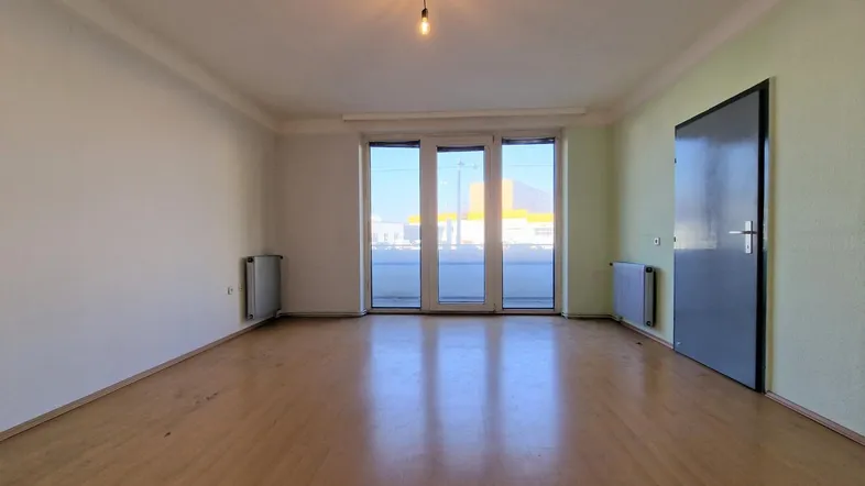Helles Wohnzimmer mit Holzboden und Zugang zu einem Balkon oder einer Loggia.