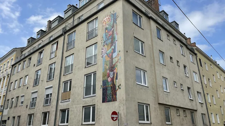 Gebäude mit einer künstlerischen Fassadenmalerei an der Ecke und mehreren Fenstern in städtischer Umgebung.