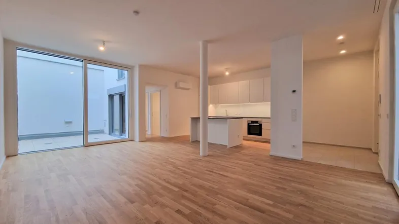 Helles, offenes Wohnzimmer mit integrierter Küche, Parkettboden und Zugang zu einer Terrasse.