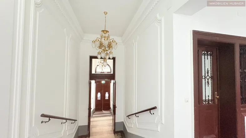 Eleganter Flur mit klassischem Kronleuchter und aufwendigen Stuckdetails an Wänden und Decke.