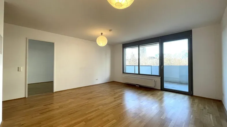 Helles Wohnzimmer mit Parkettboden, großen Fenstern und Zugang zum Balkon.