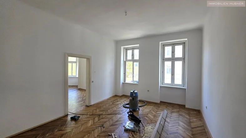 Helles Zimmer mit Fischgrätparkett und weißen Wänden, bereit für die Renovierung.