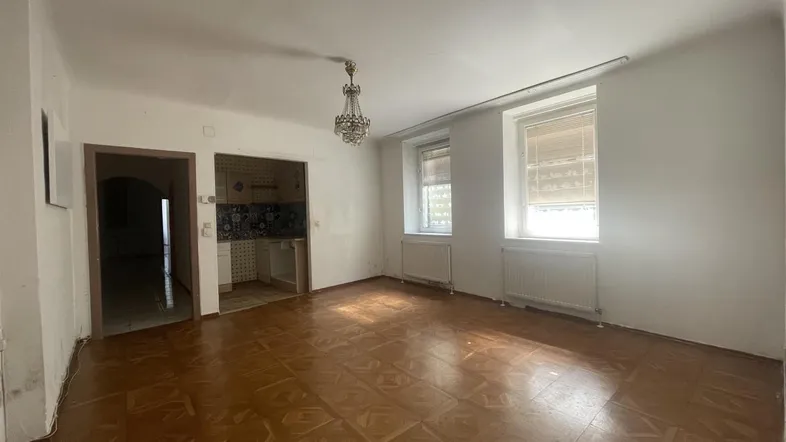Helles Wohnzimmer mit Fischgrätparkett, Kronleuchter und Zugang zu einer kleinen Küchennische.