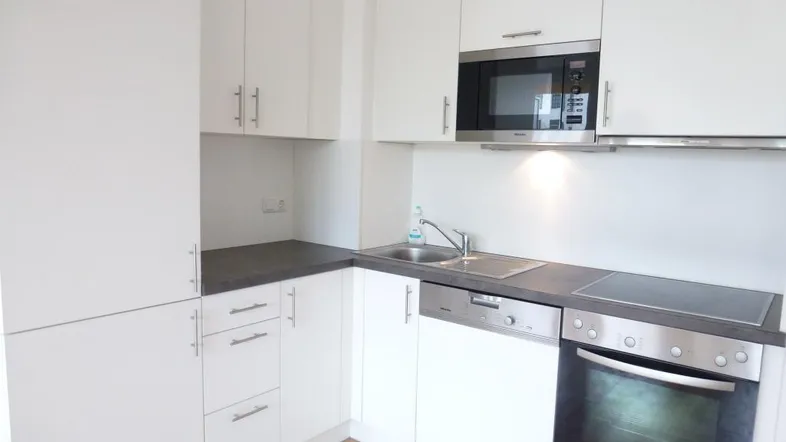 Moderne Einbauküche mit weißen Schränken, dunkler Arbeitsplatte und integrierten Geräten.