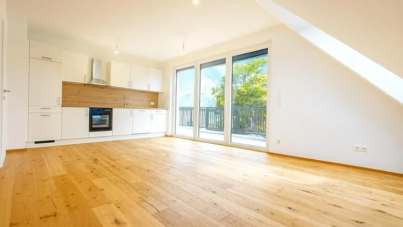 Heller offener Wohn-Essbereich mit moderner Einbauküche, Holzboden und Zugang zur Terrasse.