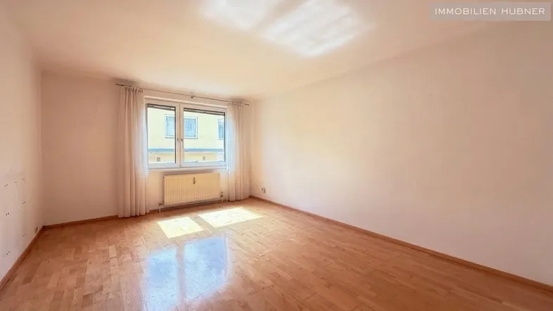 Helles Zimmer mit Parkettboden und großem Fenster, das viel Tageslicht hereinlässt.