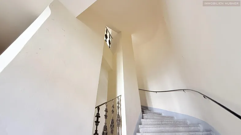 Helles Treppenhaus mit geschwungener Steintreppe und schmiedeeisernem Geländer in einem Altbau.