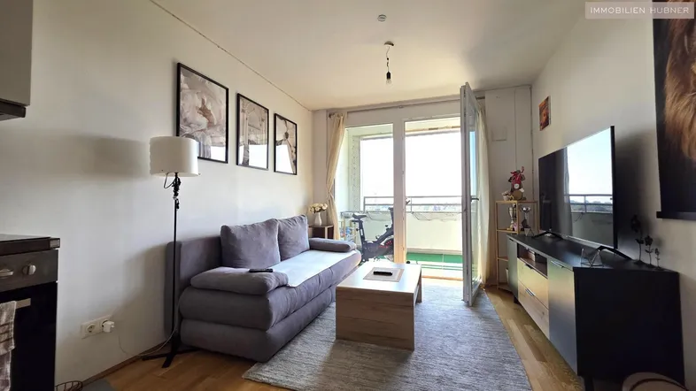 Heller Wohn-Essbereich mit Sofa, Fernseher und Zugang zu einem Balkon.
