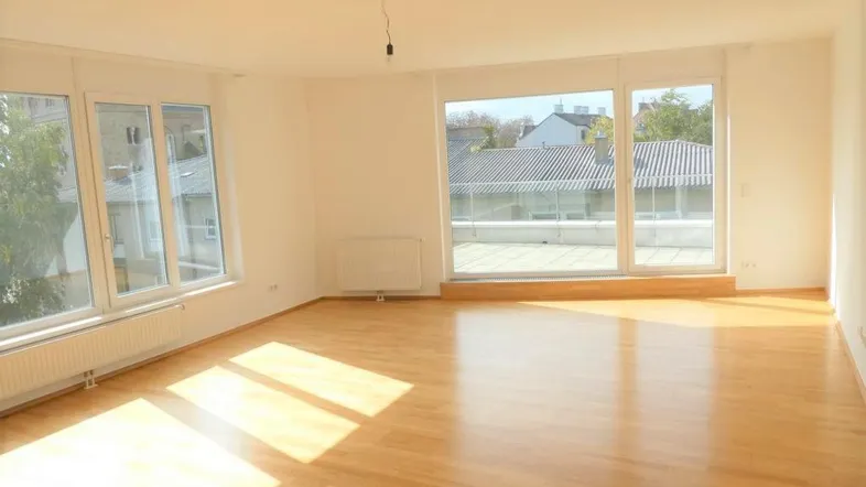 Helles Wohnzimmer mit Parkettboden und großen Fenstern, die viel Tageslicht hereinlassen.