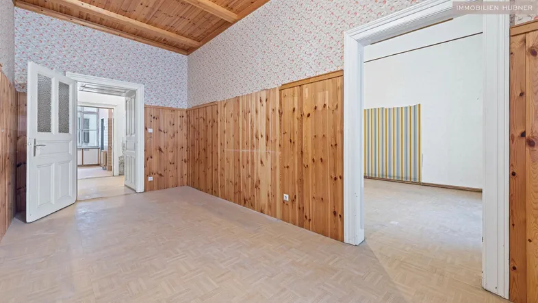 Geräumiger Innenraum mit Holzvertäfelung, gemusterter Tapete und Parkettboden, der renovierungsbedürftig ist.