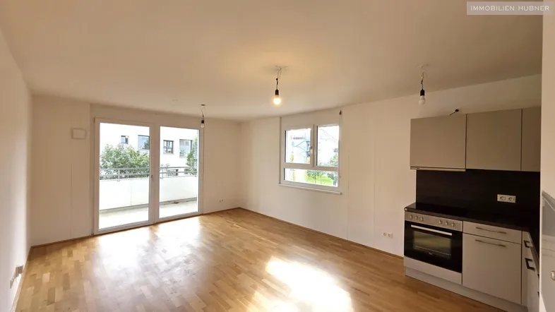 Helles Wohnzimmer mit integrierter Küchenzeile, Parkettboden und Zugang zum Balkon.