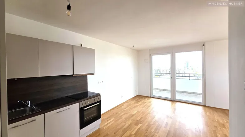 Heller offener Wohn-Essbereich mit integrierter Küche, Parkettboden und Zugang zu einem Balkon.