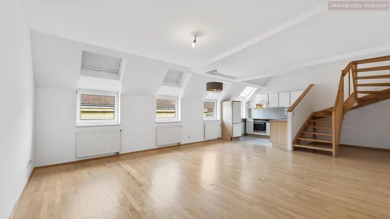 Helles Dachgeschoss-Apartment mit offener Wohnküche, Parkettboden und Holztreppe zum oberen Bereich.