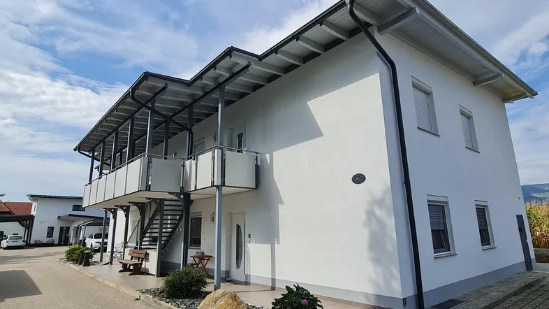 Modernes weißes Mehrfamilienhaus mit Balkonen und gepflegtem Eingangsbereich unter blauem Himmel.