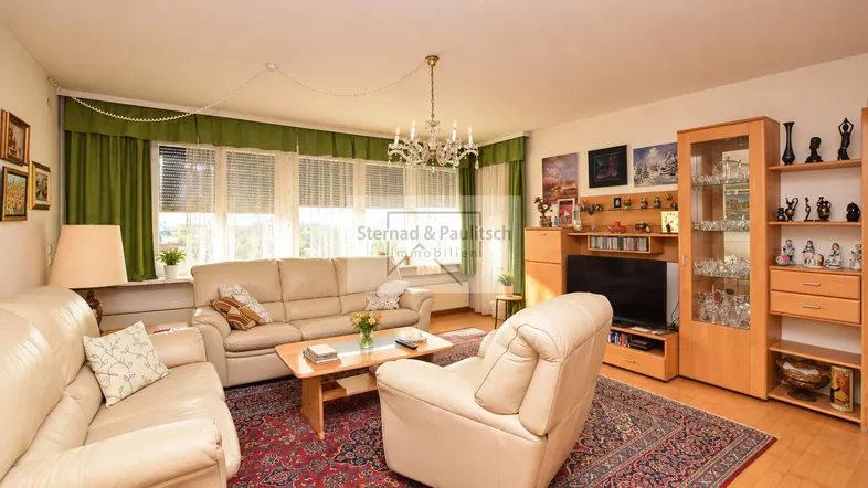 Gemütliches Wohnzimmer mit beigen Ledersofas, einem Kronleuchter und Blick ins Grüne.