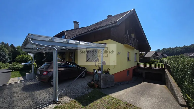Hausfassade mit Carport und Zufahrt zur Tiefgarage unter strahlend blauem Himmel.