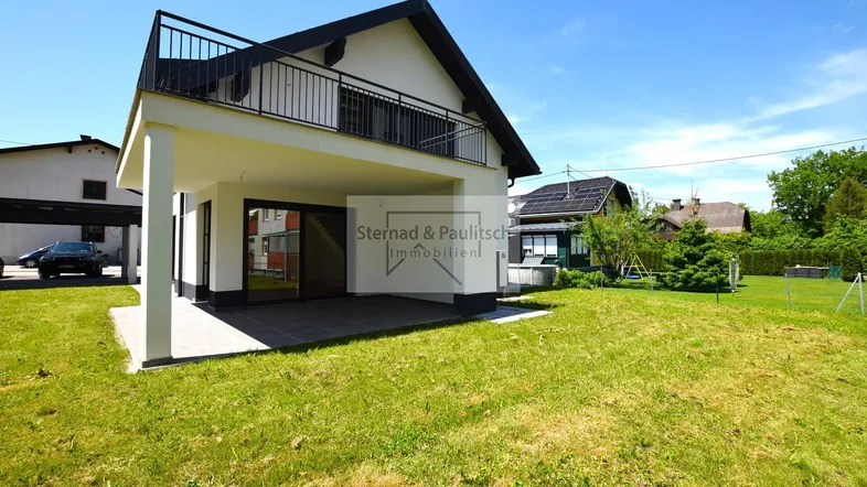 Modernes Einfamilienhaus mit großem Garten und Terrasse unter blauem Himmel.