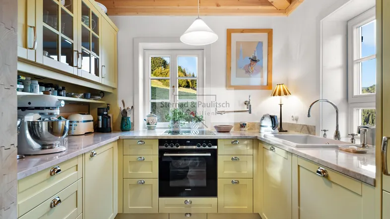 Helle Küche im Landhausstil mit gelben Schränken, Holzbalkendecke und Blick ins Grüne.
