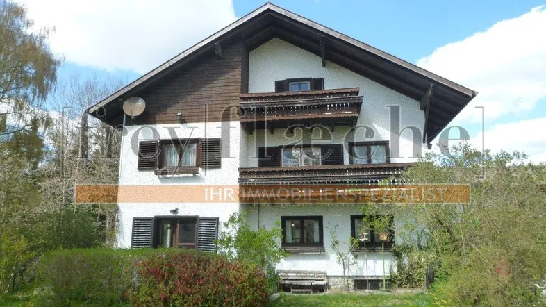 Traditionelles Haus mit weißer Fassade, Holzdetails und mehreren Balkonen in ländlicher Umgebung.