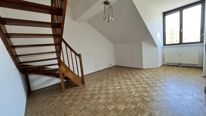 Heller Wohnbereich im Dachgeschoss mit Holztreppe, Parkettboden und schrägen Wänden.