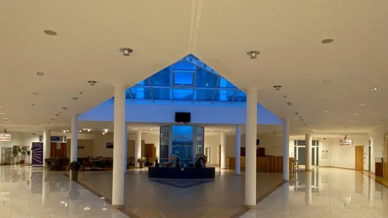 Geräumige und helle Lobby mit hoher Decke, Glasdach und dekorativem Fliesenboden in einem modernen Gebäude.