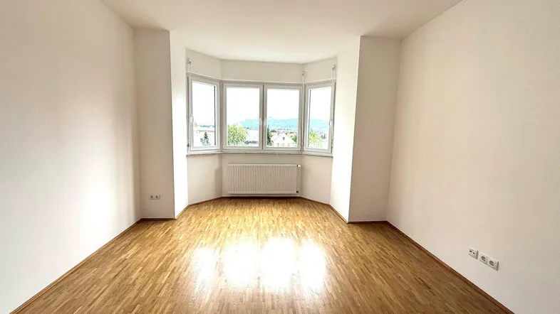 Helles, leeres Zimmer mit Erkerfenstern und Parkettboden, bietet einen weiten Blick nach draußen.