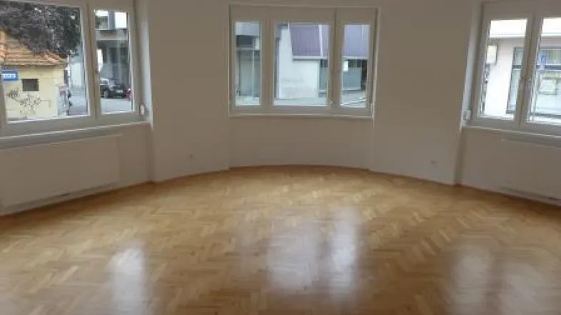 Helles, leeres Zimmer mit Fischgrätparkett und mehreren Fenstern, bereit zur Einrichtung.