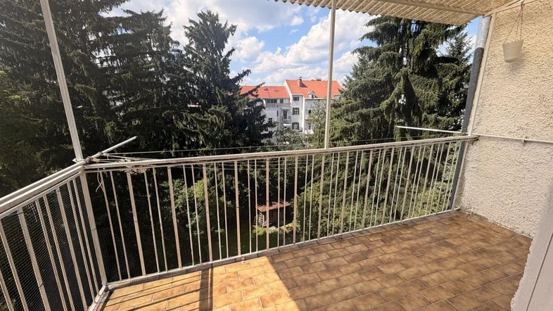 Balkon mit Fliesenboden und Blick ins Grüne sowie auf umliegende Gebäude.