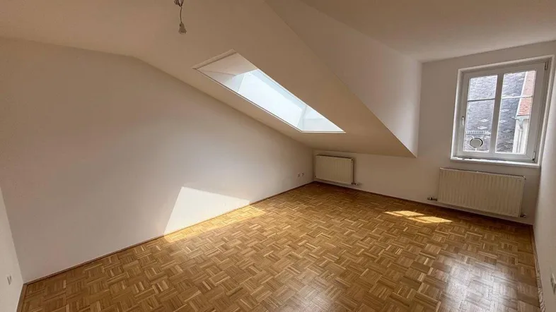 Helles Schlafzimmer im Dachgeschoss mit Parkettboden, Dachfenster und Heizkörper.