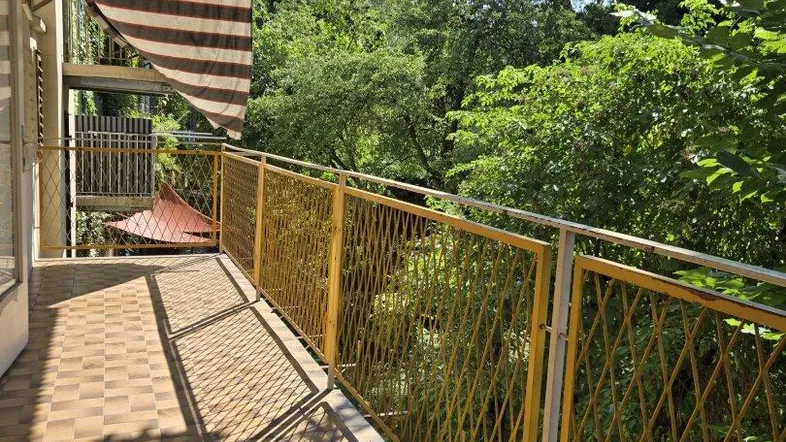 Langer, sonniger Balkon mit Fliesenboden, gelbem Geländer und Blick ins Grüne.