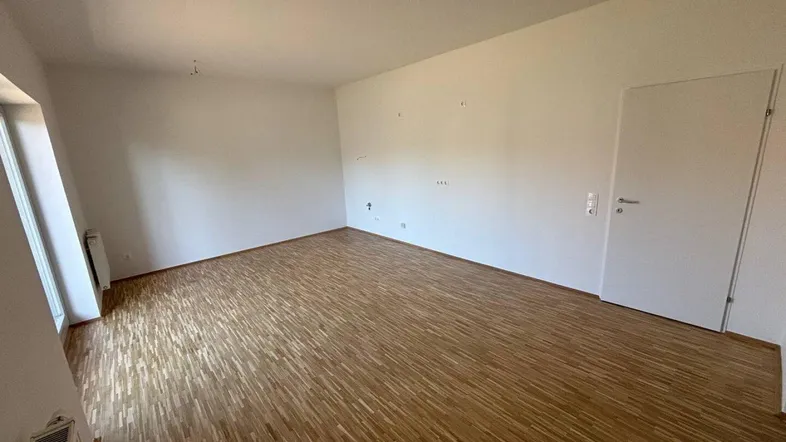 Helles, leeres Zimmer mit Parkettboden und weiß gestrichenen Wänden, bereit zur individuellen Gestaltung.