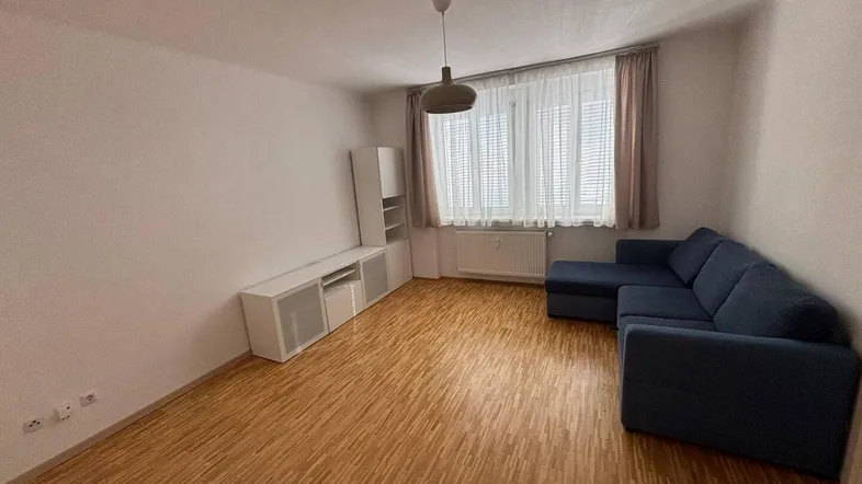 Helles Wohnzimmer mit Parkettboden, blauer Couch und Fenster mit Vorhängen.