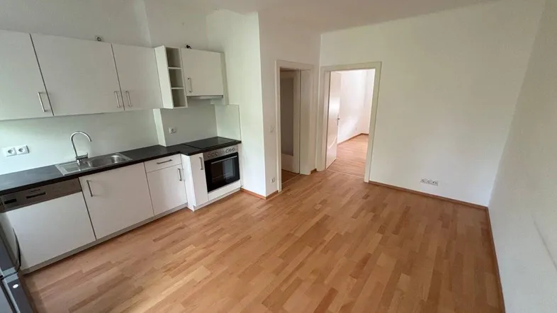 Helle Küche mit weißen Schränken, dunkler Arbeitsplatte und Holzfußboden, offen zu einem weiteren Raum.