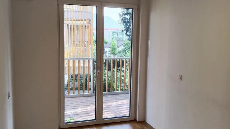 Helles Zimmer mit Holzboden und Zugang zu einem Balkon, ideal als Schlaf- oder Arbeitszimmer.