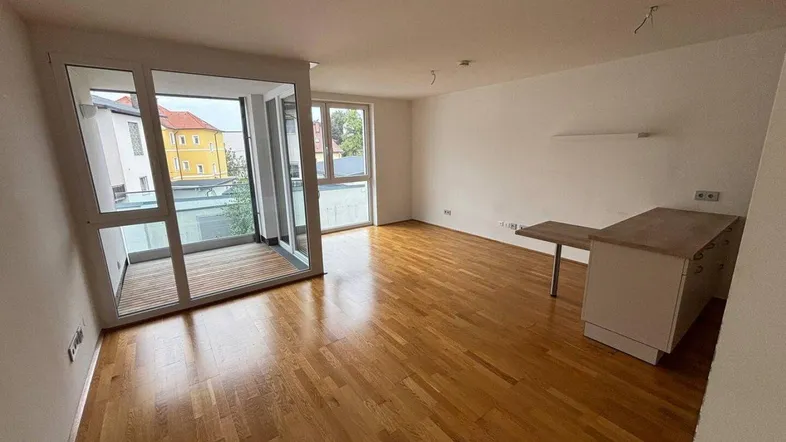 Helles Wohnzimmer mit Parkettboden, weißen Wänden und Zugang zu einem Balkon.
