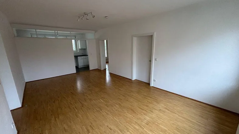 Heller Wohnbereich mit Parkettboden und offenem Übergang zu einem weiteren Raum, ideal für modernes Wohnen.