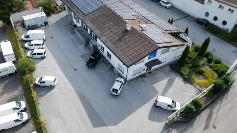 Drohnenaufnahme eines Gewerbegebäudes mit Solaranlage auf dem Dach und umliegenden Parkplätzen.