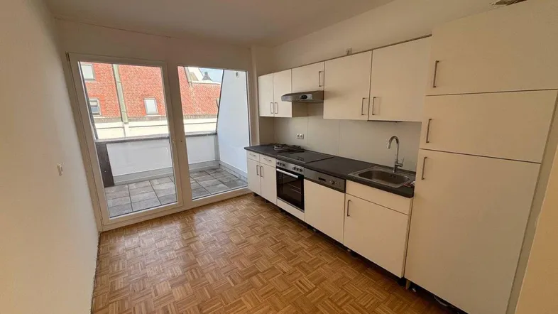 Kleine Küche mit weißen Schränken, Parkettboden und direktem Zugang zum Balkon.